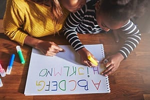 Black mother helping child write out the alphabet