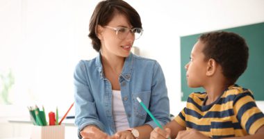 Caucasian teacher assisting young African American male student on assignment