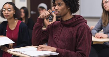 Students sitting at their desks in a classroom, a black male student at the foreground