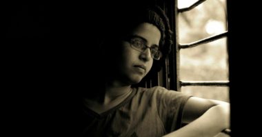 Young boy looks outside of window with gloomy look on face