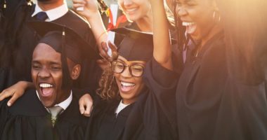 Group of diverse college students wearing gap and gowns celebrating graduation