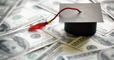 A graduation cap on top of one hundred dollar bills