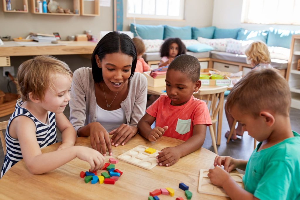 Black teacher teaching preschool students at a table