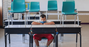 Male student sitting alone in classroom with mask on