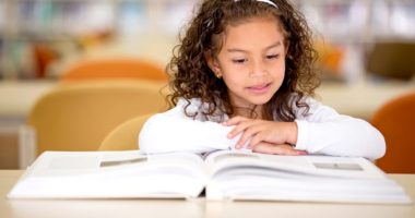 Young girl reading a book at a table in a library