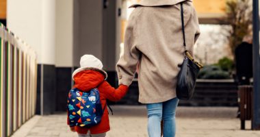 A mother holds a child's hand whilst walking outside.