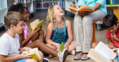 Young students on the floor listening to a teacher read a book