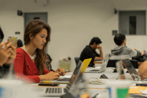 Female student working on a laptop with other students in the background