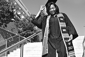 Black female graduate in cap and gown walking down stairs