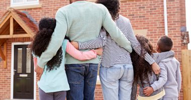 Back view of a black family embracing each other in front of a house