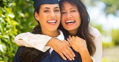 Female graduate in cap and gown embraced by older female