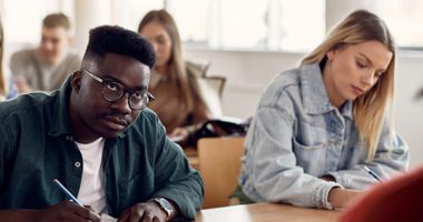 Students writing down while sitting on desks in a classroom